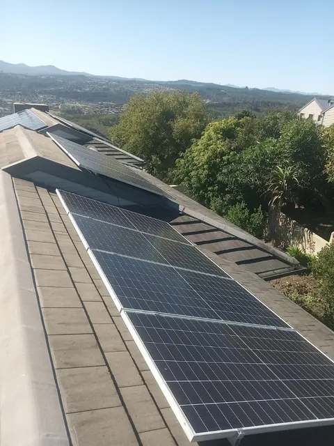 Solar panels split across two roof pitches in Knysna, framed by trees and green hills