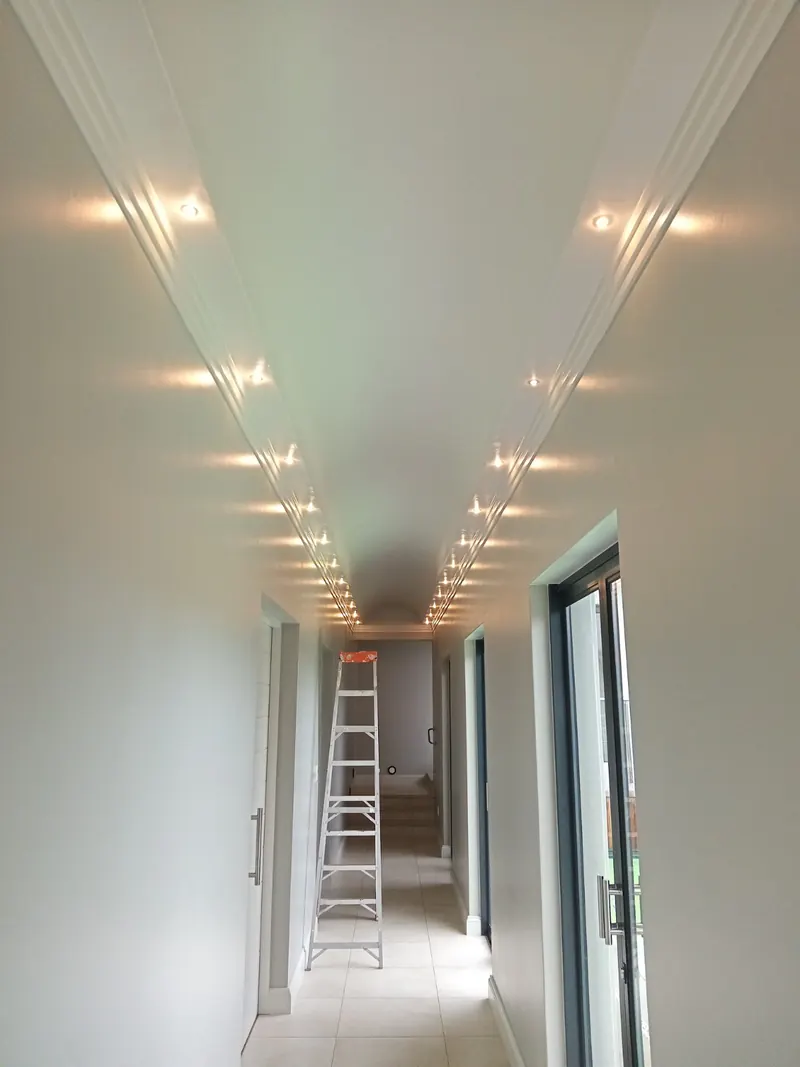 A long white corridor lit by two rows of recessed downlights set into the ceiling cornices
