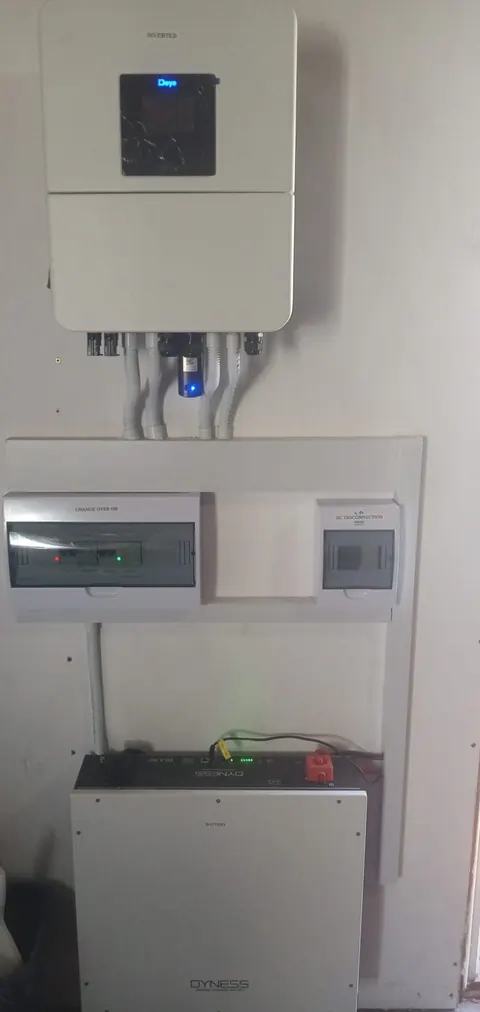 An inverter on a white backing board above a labelled change-over DB and DC disconnection box, with a lithium battery below