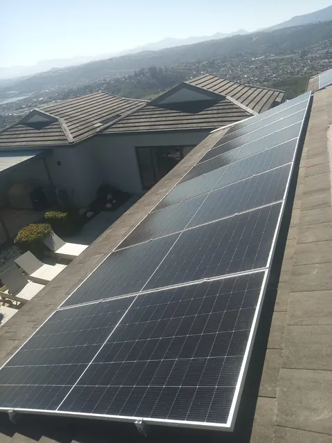 A long row of solar panels along a grey tile roof in Knysna, with the valley and mountains beyond