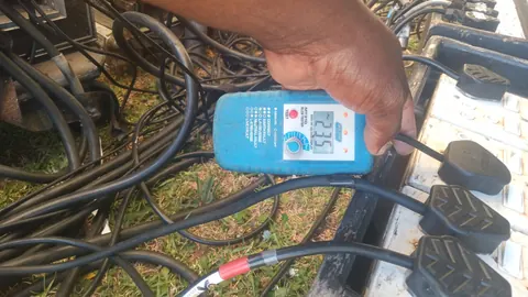 A hand holding a plug-in socket tester that reads 235 volts, plugged into a row of extension leads